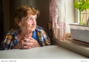 Old lonely woman sitting near the window in his house.